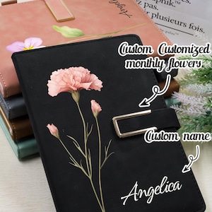 May include: Black journal featuring a pink flower design and the name "Angelica" in white script. The journal has a metal clasp and the text "Custom Customized monthly flowers" and "Custom name". Other journals are visible in the background.