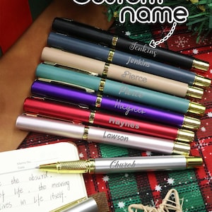 Puede incluir: Una colección de bolígrafos personalizados en varios colores, incluyendo negro, azul, turquesa, morado, rojo y plateado, cada uno grabado con un nombre. Los bolígrafos tienen detalles dorados y están dispuestos sobre un fondo a cuadros festivo. El texto "Custom name" está en la parte superior.
