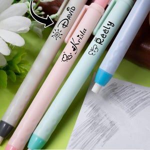 May include: A collection of personalized erasers in pastel colors: gray, pink, mint green, and light blue. Each eraser has a name printed on it in black, such as "David" and "Krista", along with decorative icons. The image also includes a custom name label.