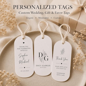 May include: Three white oval tags with rounded ends and white string loops. The tags feature black printed text and floral graphics. One tag reads "THANK YOU FOR CELEBRATING WITH US! Sophia & Michael 05.24.2025", another "DG DOCE GLAMOUR BOUTIQUE", and the third "Thank You MADE WITH LOVE JUST FOR YOU HANDMADE WITH CARE".