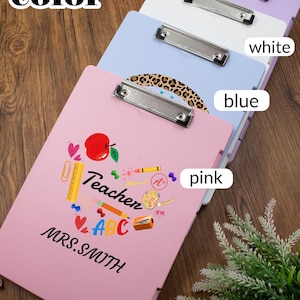 May include: A stack of colorful clipboards in pink, blue, white, and purple. The pink clipboard features the word "Teacher" with school-themed graphics and the name "MRS. SMITH". Each clipboard has a silver metal clip.