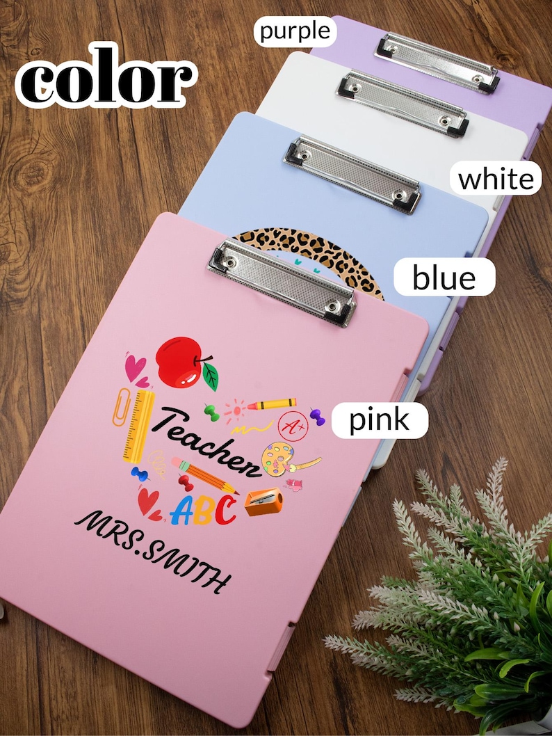 May include: A stack of colorful clipboards in pink, blue, white, and purple. The pink clipboard features the word "Teacher" with school-themed graphics and the name "MRS. SMITH". Each clipboard has a silver metal clip.