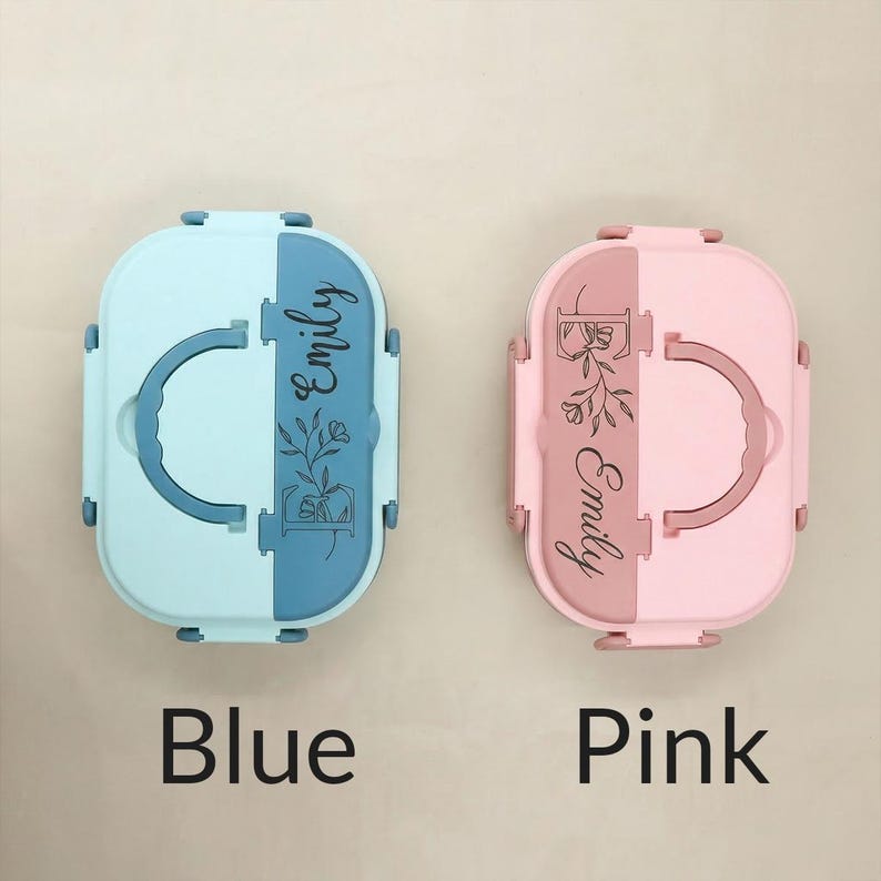 May include: Two personalized lunch boxes, one light blue and blue, the other pink and rose. Each box has a handle, a floral design, and the name "Emily" in script. The word "Blue" and "Pink" are written below the boxes.