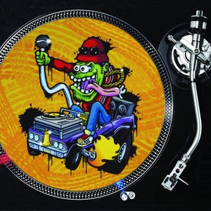 May include: A turntable featuring a vibrant cartoon graphic. The image shows a green character with red sunglasses and a red shirt, holding a microphone. The character is driving a purple car against a yellow and black background.