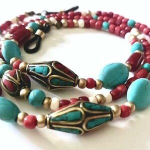 Peut inclure: Une chaîne de lunettes perlée composée de perles ovales couleur turquoise, de perles cylindriques rouge foncé, de petites perles blanches et d'entretoises en métal doré. Le design inclut deux perles métalliques allongées incrustées.