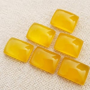 Op de afbeelding: Vijf rechthoekige cabochons gemaakt van gladde, doorschijnende gele steen. Elk stuk heeft een gepolijst, afgerond oppervlak dat licht reflecteert, met een consistente goudgele tint over alle vijf de afzonderlijke edelsteencomponenten.