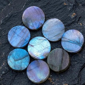 Puede incluir: Siete piedras preciosas circulares de labradorita con superficies pulidas y destellos iridiscentes en azul, morado y gris. Cada piedra muestra fracturas internas naturales y variaciones de color únicas en sus caras lisas y redondeadas.
