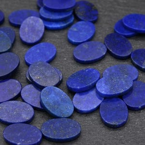 Könnte beinhalten: Eine Sammlung zahlreicher ovaler Lapis-Lazuli-Cabochons. Jedes Stück weist eine tiefe, leuchtend blaue Farbe mit verstreuten, natürlichen goldenen Pyriteinschlüssen auf den glatten, polierten Oberflächen der Steine auf.