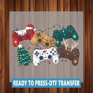 May include: A collection of colorful game controllers with holiday-themed designs, including a Santa hat, snowflakes, and reindeer antlers. A Christmas tree and string lights are also featured. The text "READY TO PRESS-DTF TRANSFER" is at the bottom.