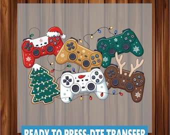May include: A collection of colorful game controllers with holiday-themed designs, including a Santa hat, snowflakes, and reindeer antlers. A Christmas tree and string lights are also featured. The text "READY TO PRESS-DTF TRANSFER" is at the bottom.