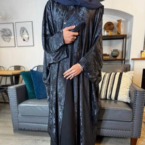 May include: A white ceramic mug with a black handle and the text "But First, Coffee" in a bold, black font. The mug is set against a blurred background, highlighting its clean design.