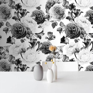 May include: A black and white floral wallpaper featuring roses and other flowers. The wallpaper is a repeating pattern of large blooms and foliage. Three vases of varying sizes and shapes are on a white surface.