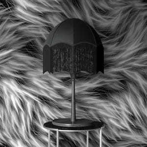May include: A black table lamp with a fringed shade, set against a textured, black and white background. The lamp has a slender stem and sits on a small, round table.