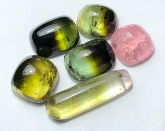 Pode incluir: Uma coleção de pedras preciosas polidas em várias formas. As pedras exibem uma gama de cores, incluindo verde, amarelo e rosa. Algumas pedras têm um efeito gradiente, com tons mais escuros transitando para tons mais claros. As pedras preciosas são exibidas em uma superfície branca.