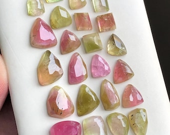 Pode incluir: Uma coleção de pedras preciosas de turmalina facetadas em várias formas e cores, incluindo rosa, verde e amarelo. As pedras preciosas são exibidas em uma superfície branca, mostrando sua clareza e brilho. Ideal para fazer joias.