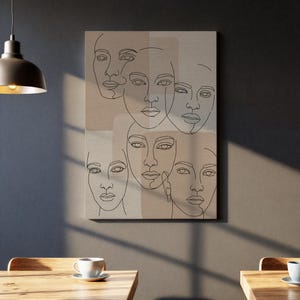 Könnte beinhalten: Ein Leinwanddruck mit einer minimalistischen Strichzeichnung von sechs Gesichtern. Die Gesichter sind in einer durchgehenden Linie dargestellt, vor neutralen beige- und beigefarbenen Farbblöcken. Das Kunstwerk hängt an einer Wand.