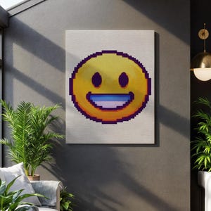 May include: A canvas print of a pixelated emoji with a yellow face, purple outline, and a wide, smiling mouth with a blue tongue. The artwork is displayed on a neutral-toned wall, adding a pop of colour to the space.