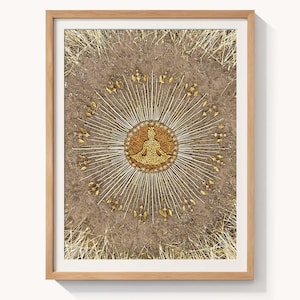 May include: Framed artwork with a central seated figure made of golden seeds, surrounded by radiating lines and decorative elements. The artwork is set against a textured brown background and encased in a light brown wooden frame. The artwork is suitable for meditation.