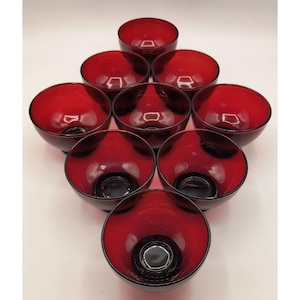 May include: A set of nine ruby red glass bowls arranged in a diamond shape. The bowls have a rounded shape with a dark, almost black, base. The interior of the bowls is a vibrant red, and the rims are smooth.