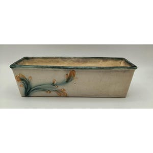 May include: Rectangular ceramic planter with a light beige exterior and a teal rim. The planter features a painted floral design in teal and orange. The planter is suitable for indoor or outdoor use.