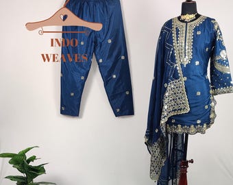 May include: A navy blue embroidered salwar kameez set. The set includes a long-sleeved tunic with gold embellishments, matching pants, and a sheer scarf. The text "INDO WEAVES" is visible on a hanger.