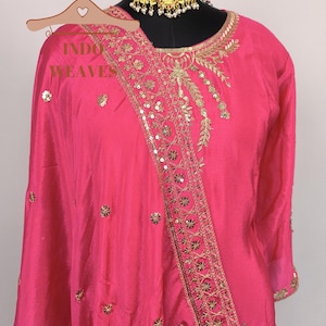 Pu&ograve; includere: Un vivace completo indiano rosa con intricati ricami dorati e abbellimenti di paillettes. Il completo presenta uno scollo tondo e maniche lunghe. &Egrave; visibile anche una collana girocollo dorata. Il testo "INDO WEAVES" &egrave; sull'appendiabiti.
