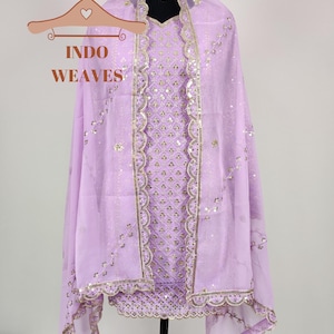 Puede incluir: Conjunto salwar kameez lila con detalles de lentejuelas y bordados dorados. El atuendo incluye una t&uacute;nica, una bufanda a juego y un collar gargantilla dorado. El texto "INDO WEAVES" es visible en una percha.