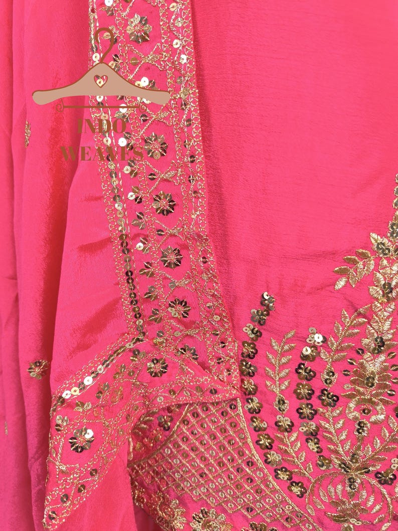 Pu&ograve; includere: Abito rosa acceso con ricami dorati e paillettes. Il design presenta motivi floreali e geometrici, creando un'estetica lussuosa e dettagliata. L'abito &egrave; esposto su una gruccia di legno.