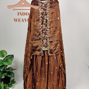 May include: A brown, formal dress with a matching shawl, displayed on a mannequin. The dress features intricate embroidery and embellishments. The text "INDO WEAVES" is visible on a hanger in the image.