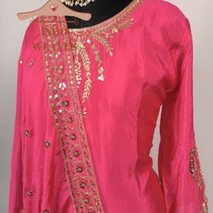 Pu&ograve; includere: Un vivace completo salwar kameez rosa con ricami dorati e paillettes. L'outfit include un top a maniche lunghe, una sciarpa abbinata e una collana dorata. I dettagli intricati aggiungono un tocco di eleganza all'abito tradizionale indiano.