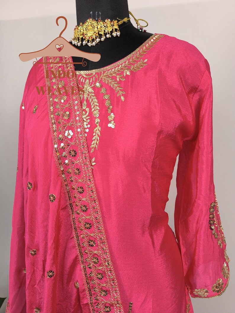 Pu&ograve; includere: Un vivace completo salwar kameez rosa con ricami dorati e paillettes. L'outfit include un top a maniche lunghe, una sciarpa abbinata e una collana dorata. I dettagli intricati aggiungono un tocco di eleganza all'abito tradizionale indiano.