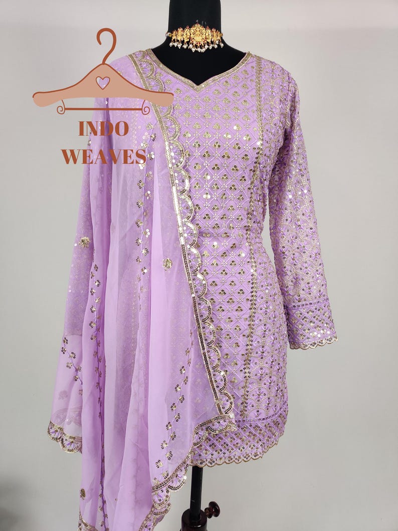 Puede incluir: Un conjunto salwar kameez lila con detalles dorados. El conjunto incluye una t&uacute;nica de manga larga, pantalones a juego y un dupatta transparente. El maniqu&iacute; muestra el bordado y el dise&ntilde;o detallados, con medidas en cent&iacute;metros.