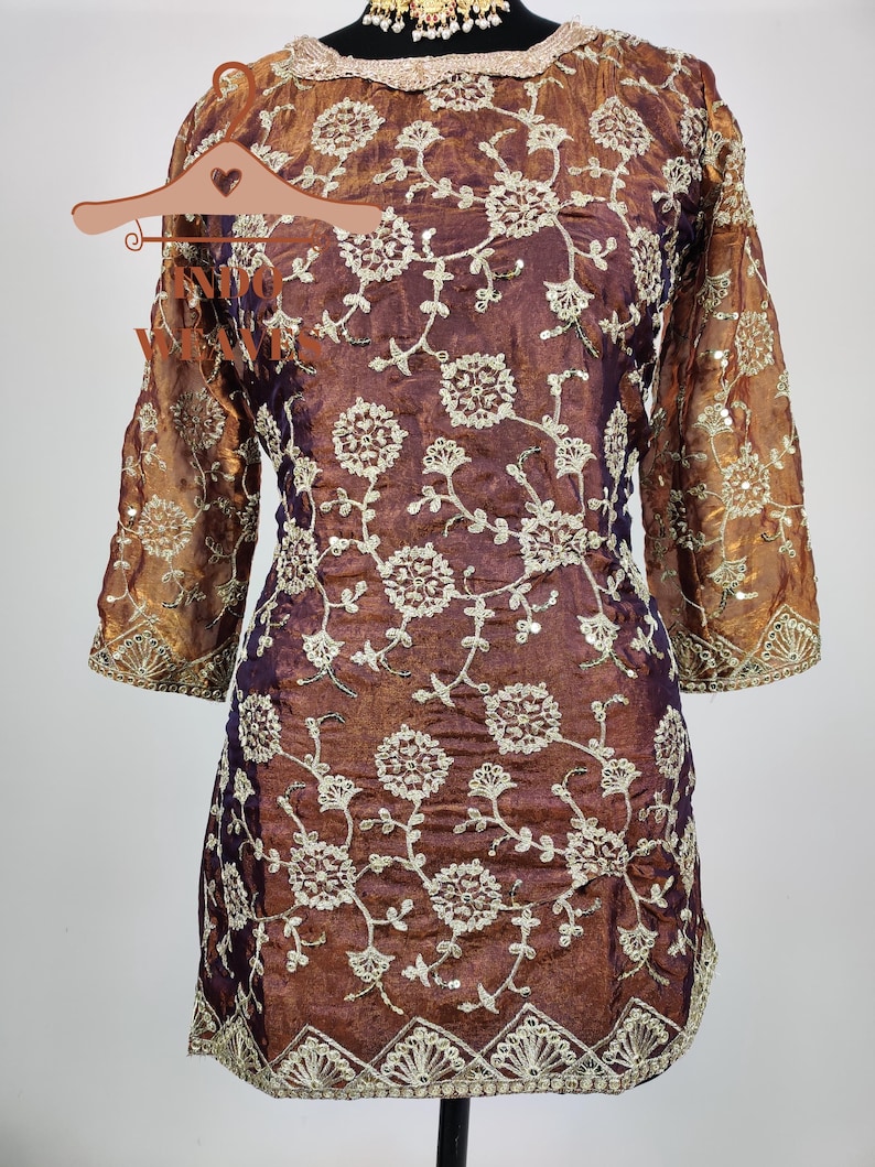 May include: A brown and purple tunic with floral embroidery. The tunic has three-quarter sleeves and a scalloped hem. The floral embroidery is in a cream color and covers the front and sleeves of the tunic.
