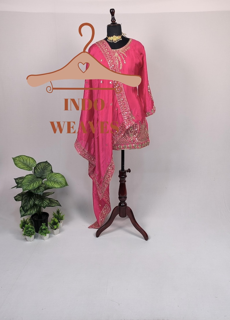 Pu&ograve; includere: Un vivace completo indiano rosa con ricami dorati e paillettes. L'outfit include una tunica e una sciarpa abbinata, esposto su un manichino. Il testo "INDO WEAVES" &egrave; visibile su un appendiabiti.