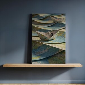 May include: A paper boat sails on a sea of maps in this artistic print. The boat is white and grey, and the maps are shades of blue, green, and tan. The artwork is displayed on a wooden shelf against a dark blue wall.