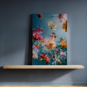 Puede incluir: Una impresión en lienzo con flores coloridas sumergidas en agua. Las flores, en tonos rosa, naranja y amarillo, están rodeadas de burbujas sobre un fondo azul. La obra de arte se exhibe en una estantería de madera.