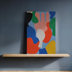 May include: Abstract canvas art featuring a light blue background with colorful shapes in red, pink, green, yellow, blue, and white. The artwork is displayed on a wooden shelf against a dark blue wall.