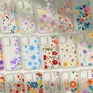 Könnte beinhalten: Eine Sammlung klarer Handyhüllen mit verschiedenen floralen Designs. Die Hüllen zeigen bunte Blumen, darunter rote, blaue, gelbe und lila, wobei einige Designs Bienen enthalten. Die Hüllen sind in Reihen angeordnet.