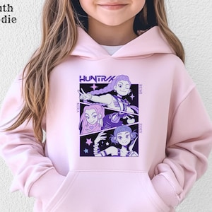 May include: Light pink youth hoodie with a graphic featuring three anime-style characters and the word "HUNTRAX". The names Mira, Rumi, and Zoey are also displayed. The hoodie has a front pocket and a hood.