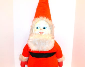 May include: A vintage Santa Claus doll with a long, pointed red hat and a white pom-pom. The doll has a white face with blue eyes, a fluffy white beard, and a red suit with a black belt and white trim. A classic Christmas decoration.