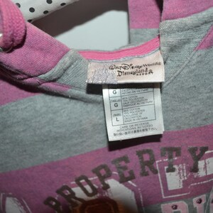 Pu&ograve; includere: Una felpa con cappuccio a righe nei toni del magenta e del grigio m&eacute;lange con coulisse. L'etichetta interna sul collo mostra il logo del Walt Disney World Disneyland Resort e un'etichetta di taglia L con i dettagli della composizione.