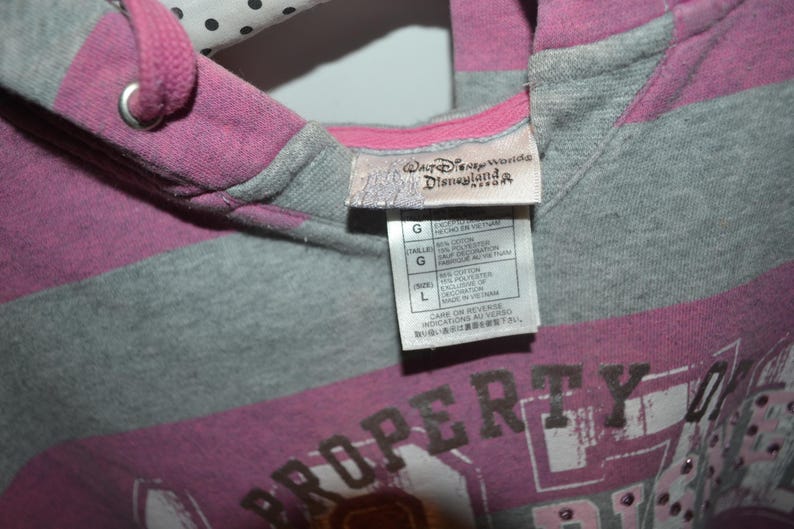 Pu&ograve; includere: Una felpa con cappuccio a righe nei toni del magenta e del grigio m&eacute;lange con coulisse. L'etichetta interna sul collo mostra il logo del Walt Disney World Disneyland Resort e un'etichetta di taglia L con i dettagli della composizione.