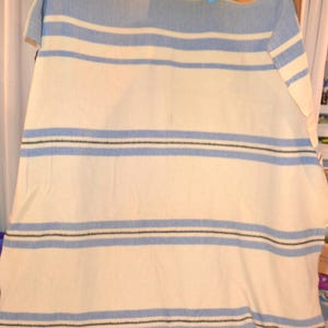 May include: A light blue and white striped blanket hanging from a wooden rod with colorful clothespins. The blanket has horizontal stripes of light blue, white, and thin black lines. The blanket is made of a soft material.