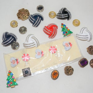 Puede incluir: Surtido de botones coloridos de diferentes formas y tamaños, incluyendo un árbol de Navidad, Papá Noel, bastones de caramelo y un trébol. Los botones están empaquetados en una bolsa de plástico transparente con una etiqueta blanca que dice "The Santa Shoe Shoppe".