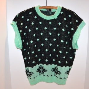 Può includere: Un maglione senza maniche nero e verde con un motivo a rombi e un design a fiocco di neve.