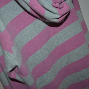 Pu&ograve; includere: Una felpa con cappuccio caratterizzata da un motivo a righe orizzontali che alterna tonalit&agrave; di grigio melange e rosa tenue. Il capo &egrave; dotato di cappuccio e maniche lunghe, con un tessuto che presenta una trama a maglia uniforme su tutto il design.