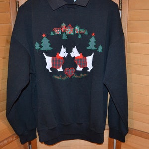 May include: Black sweatshirt with a dark gray collar featuring an embroidered holiday design. The design includes two white dogs wearing red plaid scarves, Christmas trees, houses, and a red heart. The sweatshirt has long sleeves and a crew neck.