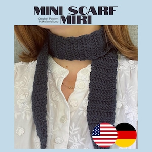 Könnte beinhalten: Ein dunkelgrauer Häkelschal mit strukturiertem Stichmuster, der um den Hals getragen wird. Das Bild enthält den Text MINI SCARF MIRI, Crochet Pattern und Häkelanleitung sowie kleine kreisförmige Symbole der amerikanischen und deutschen Flagge.