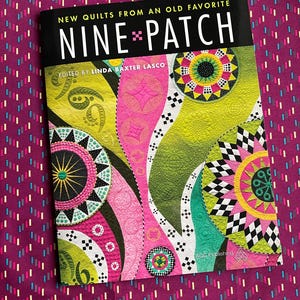 May include: A book titled "Nine-Patch" with colorful quilt designs on the cover. The cover features a black banner with white text, and the book is set against a patterned purple background. The book is edited by Linda Baxter Lasco.