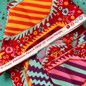 Puede incluir: Primer plano de tela colorida con fondo rojo y rayas naranja y amarillas. La tela tiene un diseño floral y el texto "for Rowan Westminster Fibers # PWGP 153 Striped Heraldic". La tela está doblada sobre un fondo turquesa.